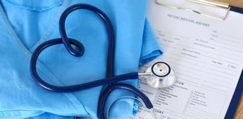 Medical stethoscope twisted in heart shape lying on patient medical history list and blue doctor uniform closeup. Medical help or insurance concept. Cardiology care health protection and prevention