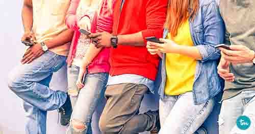 Multiracial group of friends texting sms and looking down to cell phone - Interracial students hands using mobile - Concept of young people addiction to web technology - Focus on hand of red hair girl
