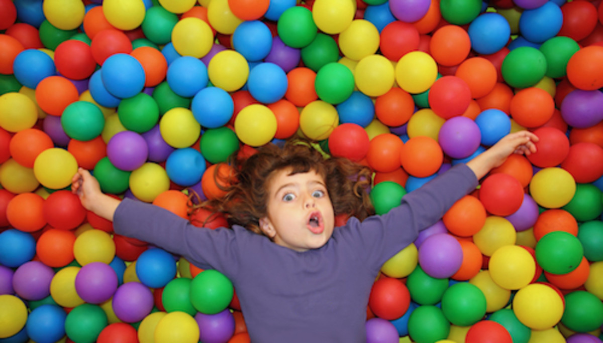 funny little girl lying over colorful balls in the park gesturing happy